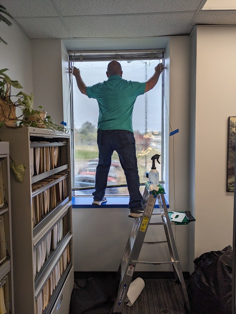 Installer on a ladder applying film to an office window