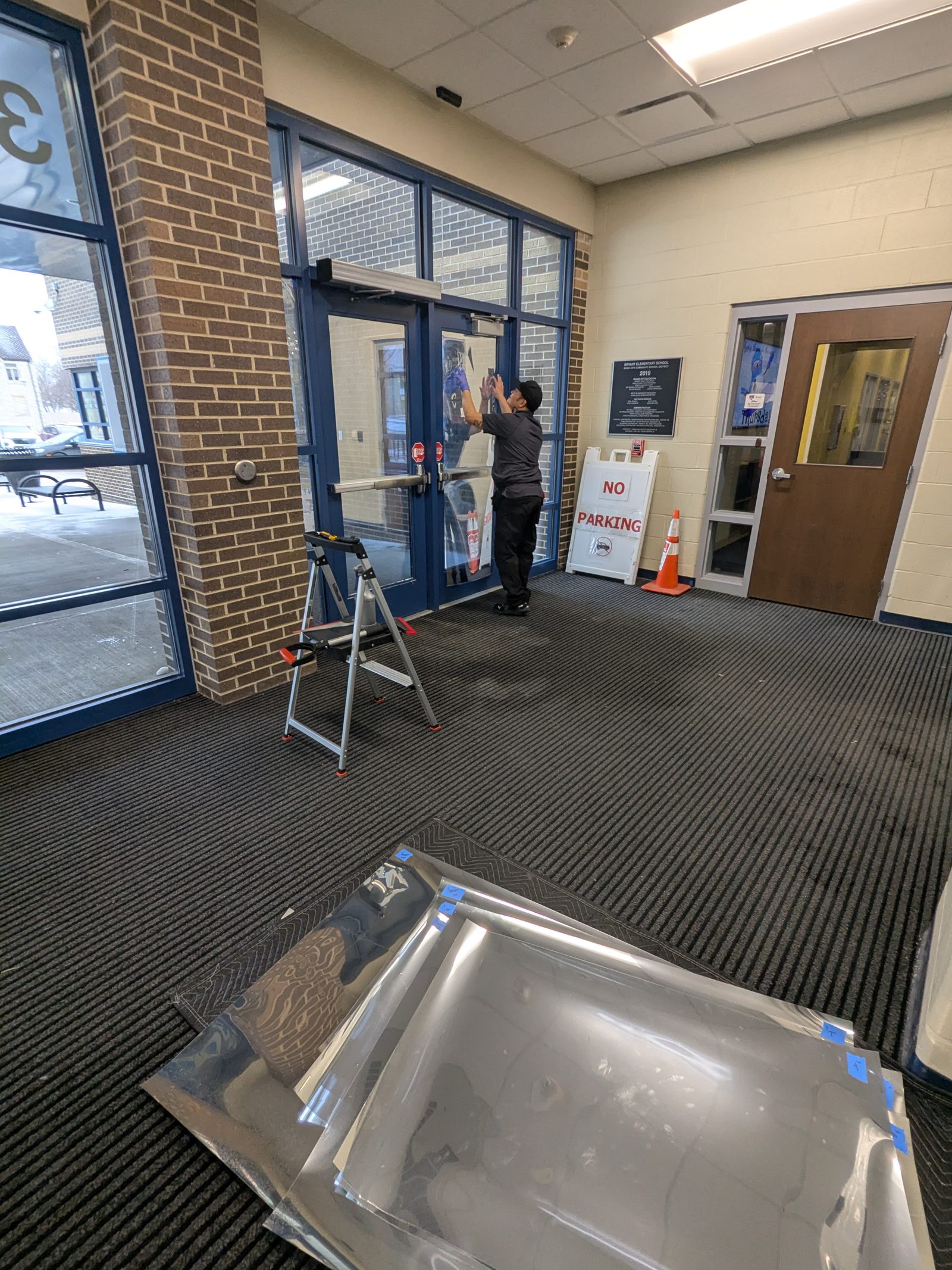 Installer working on entrance glass beside a ladder and film supplies